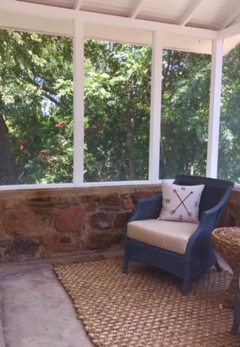 Screened in rock porch off Ratliff Suite with sitting area, blue chairs and tan rug and wicker table