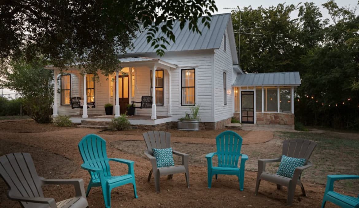 White cottage surrounded by trees with a circle of chairs out front