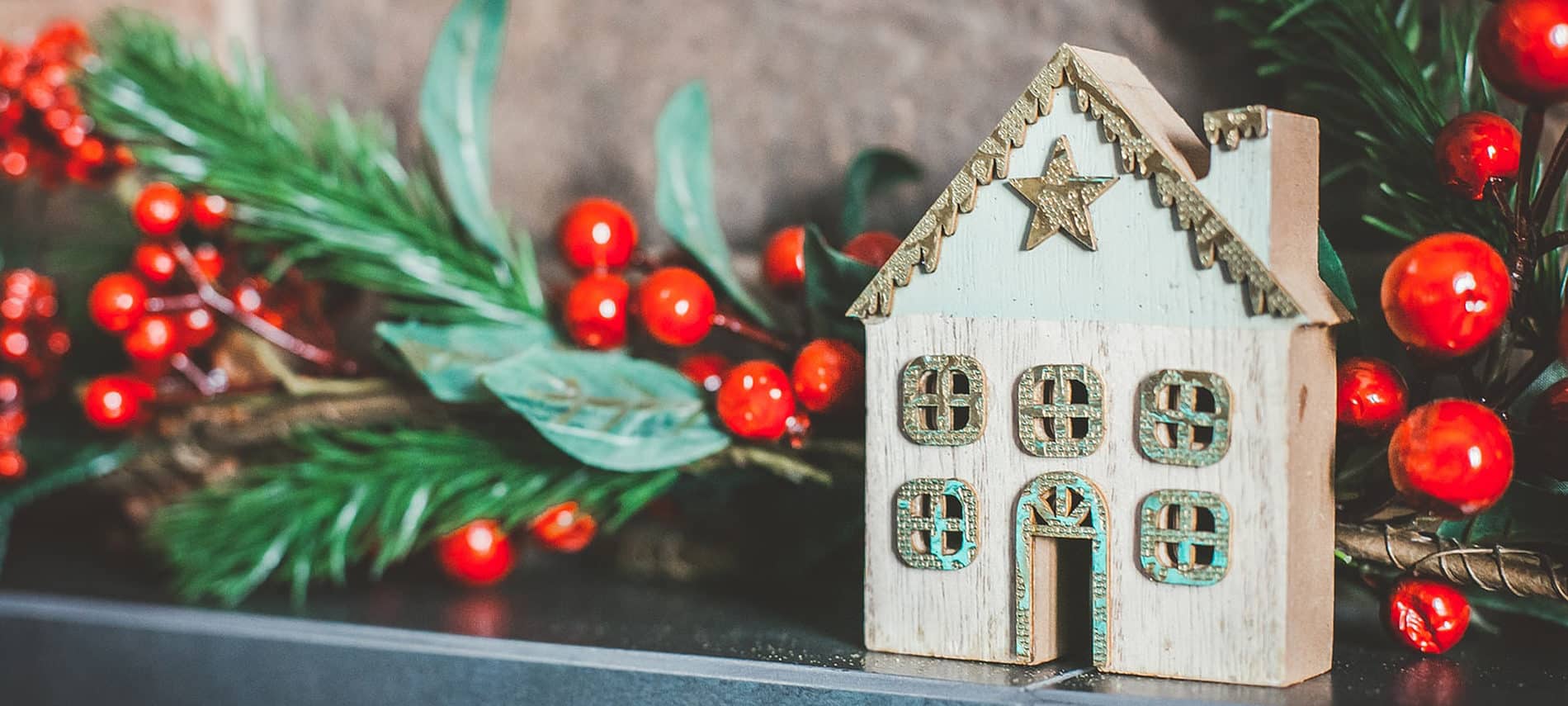 brown miniature house with star on gray stone shelf with branch of red berries and green leaves behind