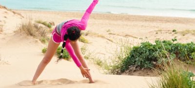 Woman in pink top doing yoga on the beach