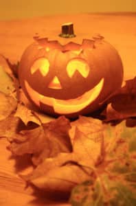 lighted Halloween carved smiling Jack O'Lantern with orange fall leaves