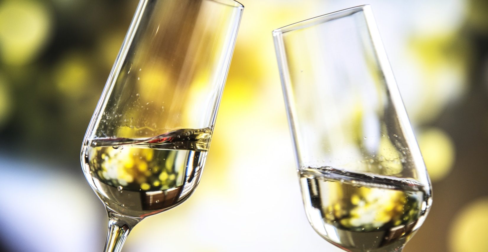 two flute glasses with white wine being toasted together