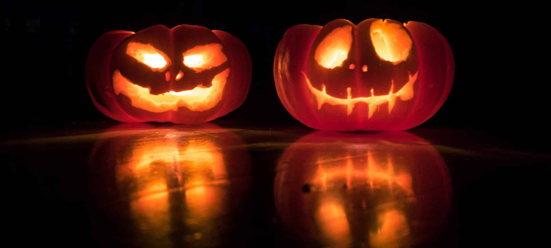 two lighted orange jack o'lanterns reflecting on black surface